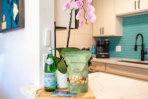 A kitchen counter with a bottle of Pellegrino water, a bag of Honolulu Cookie Company mini bites, a thank you card, and a potted orchid. - Hip Hawaiian Oceanfront Vistas (Kihei)