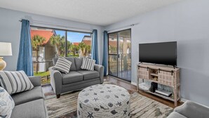 Ein modernes Wohnzimmer mit grauem Sofa, Hocker und einem TV-Schrank mit Flachbildfernseher.