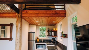 A modern kitchen with wooden beams, white cabinets, and a large island. - The Treehouse at Hulili Farm - NEW  (Hakalau)