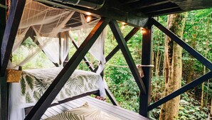 A wooden deck with a bed and a hanging chair, surrounded by lush greenery. - The Treehouse at Hulili Farm - NEW  (Hakalau)