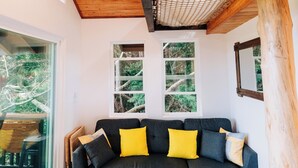 A cozy room with a dark gray sectional sofa, wooden beams, and a ceiling fan. - The Treehouse at Hulili Farm - NEW  (Hakalau)