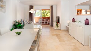 A modern, well-lit room with a dining table, chairs, a sofa, and a kitchen area. - Los Lagos de Santa Maria by Interhome (Elviria, Marbella)