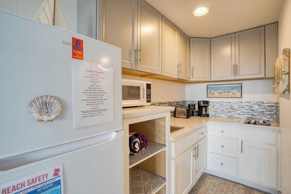 A kitchen with white cabinets, a microwave, a sink, and a countertop with a coffee maker.