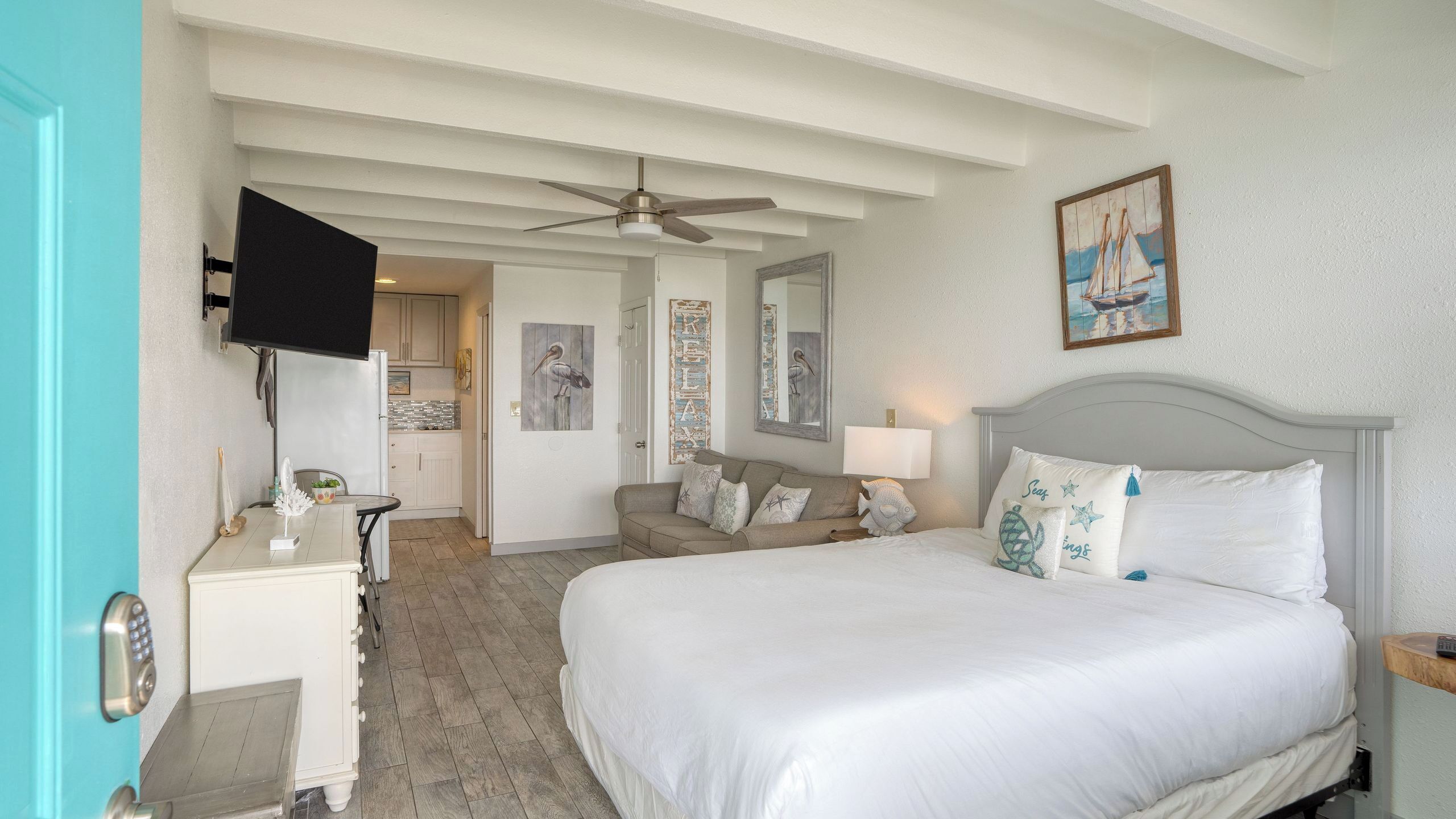 A bedroom with a bed, a sofa, a TV, a ceiling fan, and artwork on the walls.