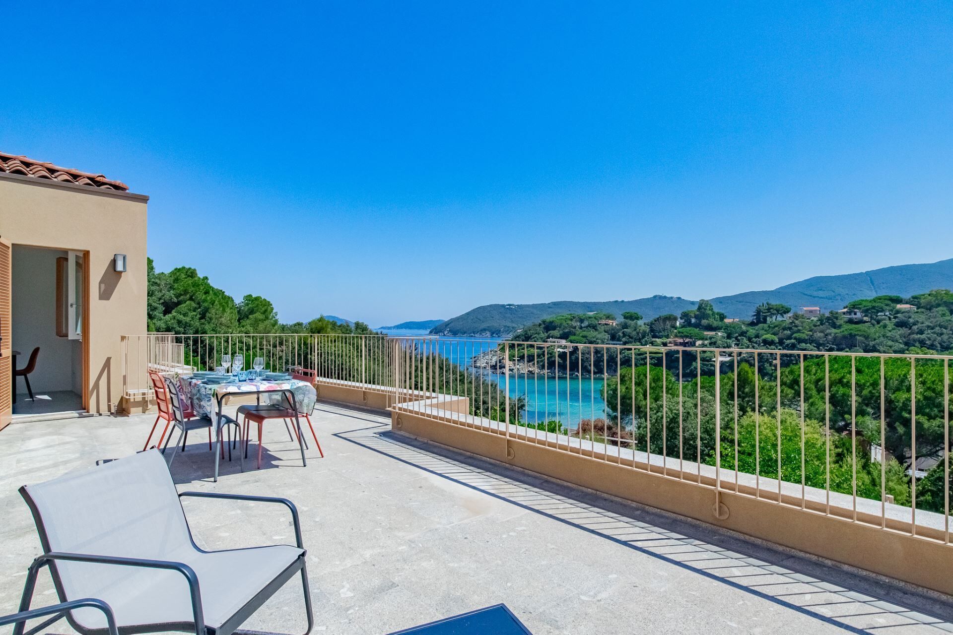 Ein Balkon mit Tisch und Stühlen, der Blick auf eine Küstenlandschaft mit Bergen im Hintergrund bietet.