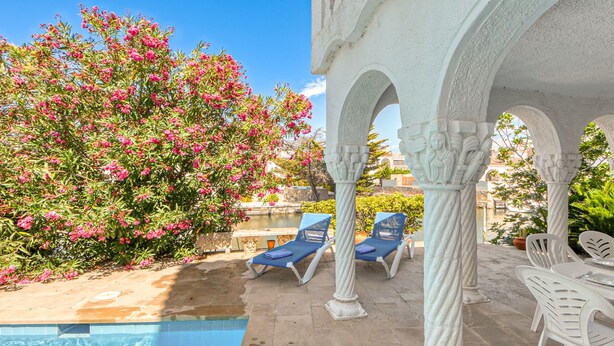 A poolside area with a clear view of the pool, blue lounge chairs, and white columns. - Vacation home Playa by Interhome (Empuriabrava)