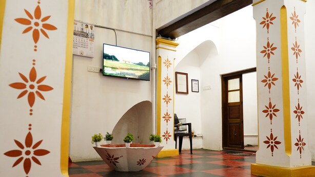A hallway with a checkered floor, decorative columns, a television mounted on the wall, and a door in the background. - White Town Villa  (Puducherry)
