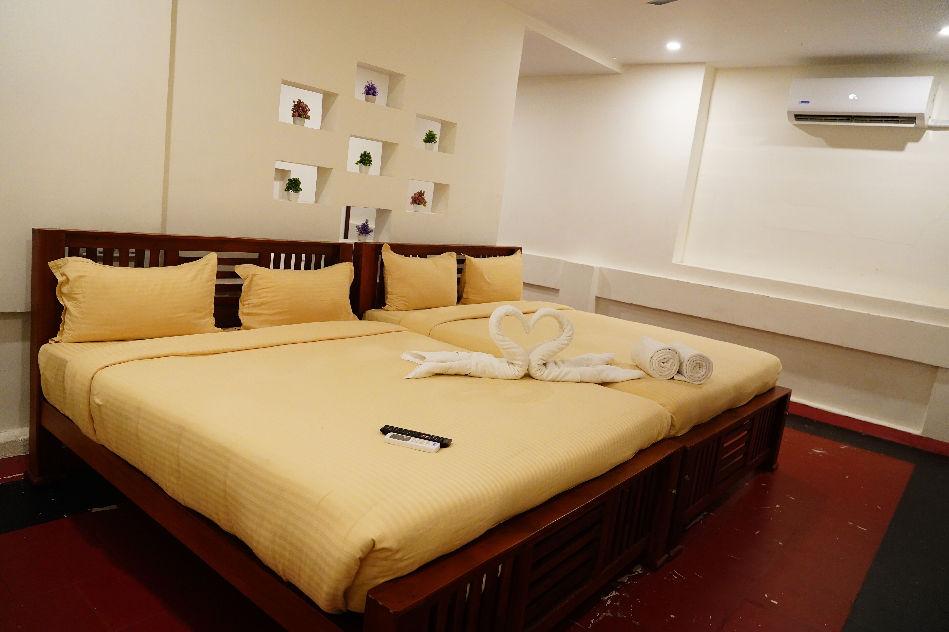 Una cama bien tendida con un control remoto encima, un aire acondicionado de pared y varios pequeños maceteros en la pared.