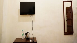 A room with a mounted flat-screen TV, a wall-mounted air conditioner, a wooden table with a kettle, a bottle of water, and a remote control. - White Town Villa  (Puducherry)