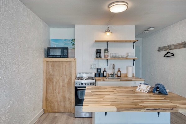 A compact kitchen with a wooden countertop, a stove, and a microwave. - Sun-kissed by Avantstay Beachfront Access (Panama City Beach)