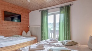 Habitació amb dos llits, sostre de fusta, finestra amb cortines verdes i un radiador.