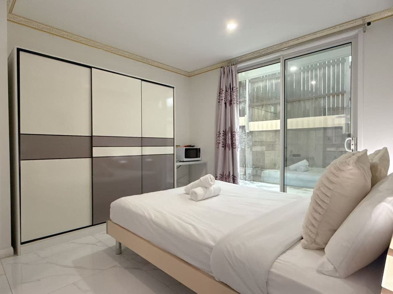 A bedroom with a bed, a wardrobe, a television, and a window with curtains.