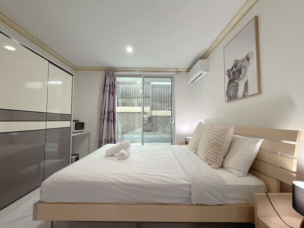 A bedroom with a bed, a bedside table, a wardrobe, a window with curtains, and a wall-mounted air conditioner.