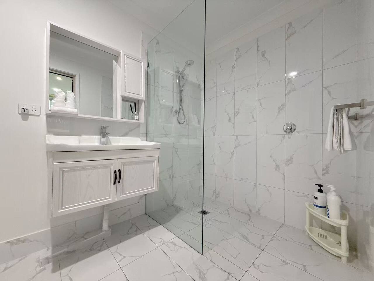 Une salle de bain moderne avec une douche à parois de verre, un meuble-lavabo blanc avec un miroir et une petite étagère contenant des articles de toilette.