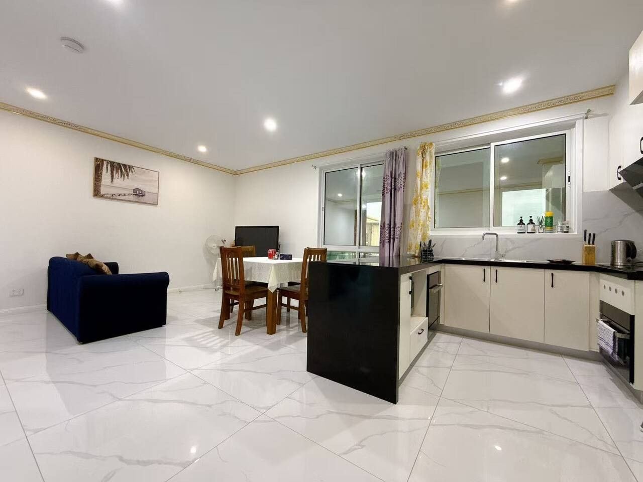 A modern kitchen with a dining area, a sofa, and a window with curtains.