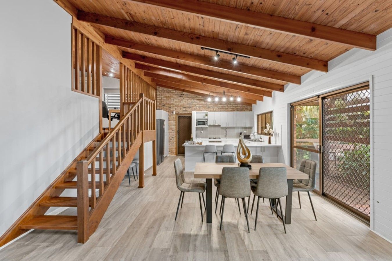 A modern kitchen with a brick wall, wooden ceiling beams, and a dining area with a table and chairs.
