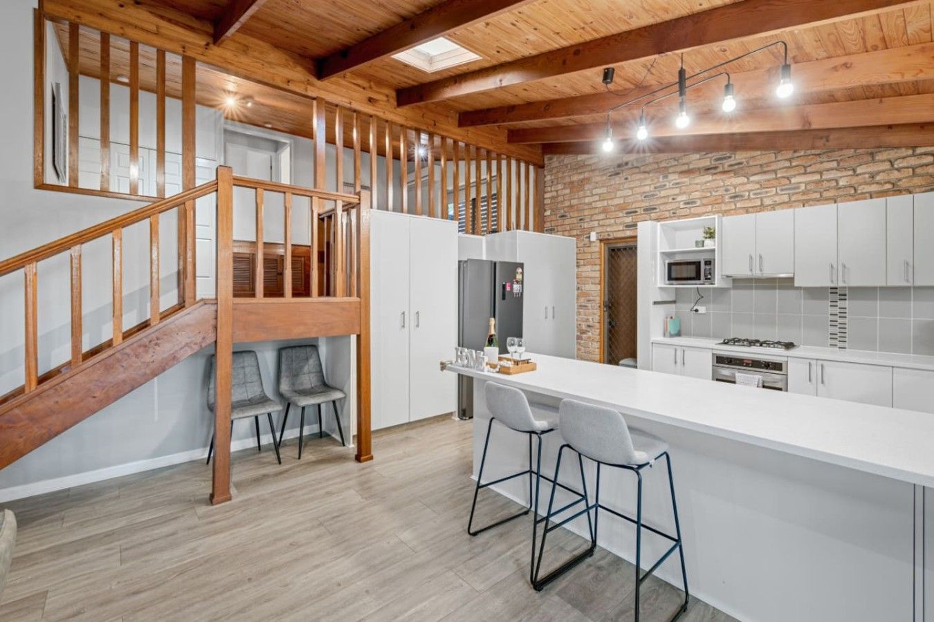 A modern kitchen with a wooden staircase, white cabinets, and a bar area.