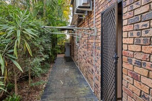 A narrow brick pathway leading to a gated entrance with a metal gate and a small utility box.