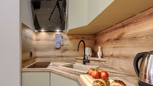 Een moderne keuken met een houten spatwand, een inbouwspoelbak, een waterkoker en een snijplank met tomaten en croissants.