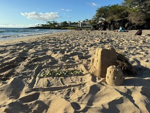 A sandy beach with footprints and a sandcastle, a clear sky, and buildings in the background.