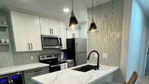 Een moderne keuken met witte kastjes, roestvrijstalen apparatuur, een marmeren eiland en twee barkrukken.