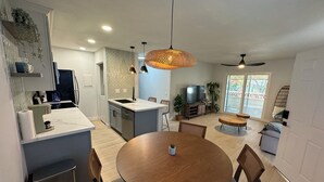 Een moderne keuken met een centraal eiland, een eetgedeelte met een ronde tafel, en een zithoek met televisie.