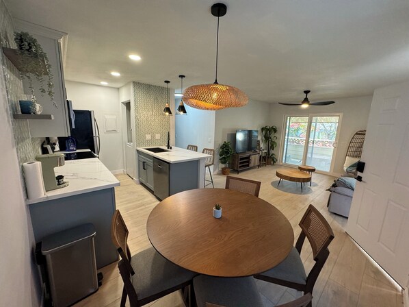 A modern kitchen with a central island, a dining area with a round table, and a living space with a TV and seating.