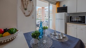 A modern kitchen with white cabinets, a black microwave, and a small oven. A dining table with a blue tablecloth and white placemats is set with cups and a vase of flowers.