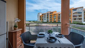 A balcony with a table set for dining, overlooking a building with balconies and a clear sky.