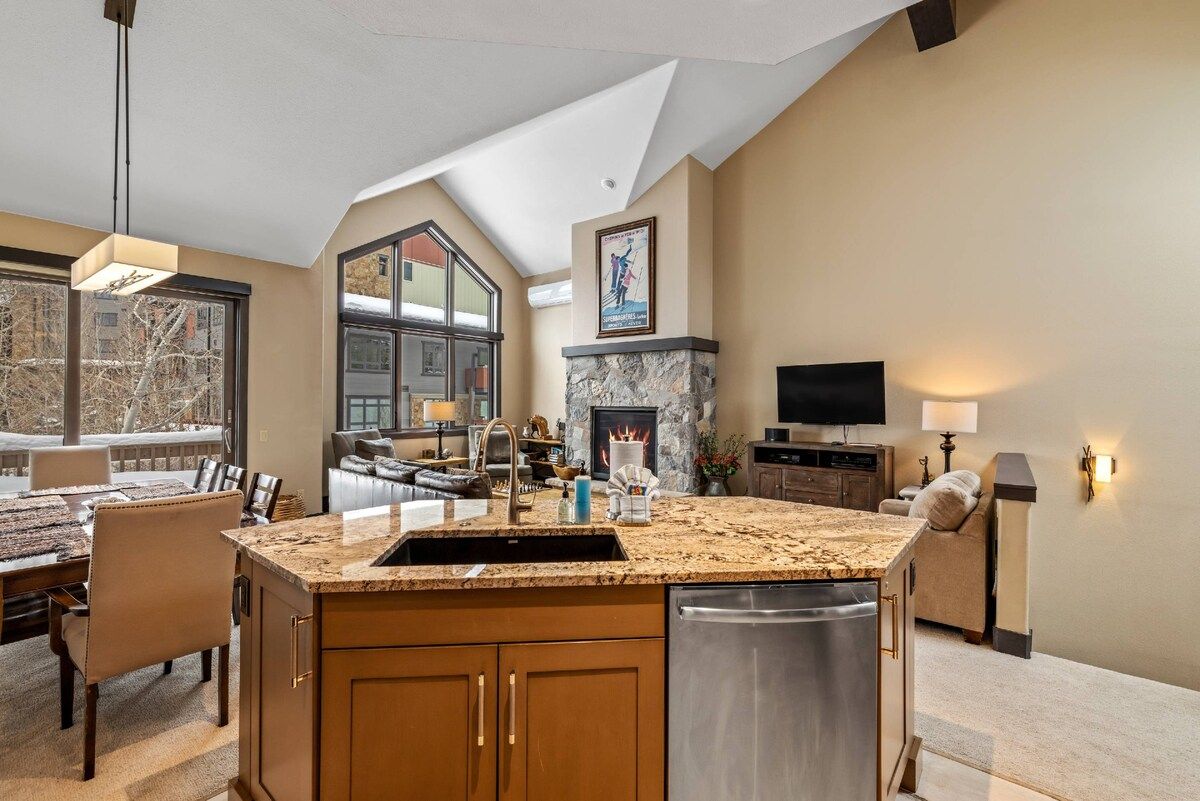 A kitchen with a large island, a fireplace, and a dining area with a view.