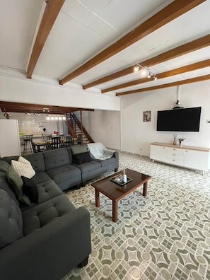 A living room with a sectional sofa, a coffee table, a TV, and a staircase leading to a dining area.