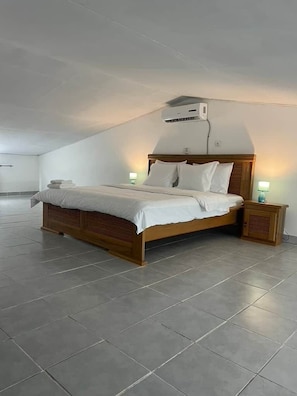 A bedroom with a wooden bed, a nightstand, a wall-mounted air conditioner, and a tiled floor.
