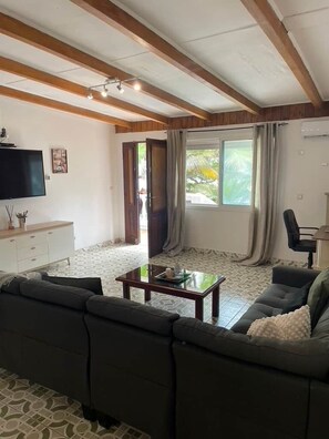 A living room with a sofa, a coffee table, a TV, and a window with curtains.