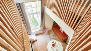 Un intérieur moderne avec un plafond en lambris de bois, une table ronde blanche avec un plateau en verre, un canapé rouge et une vue sur la verdure à l’extérieur.