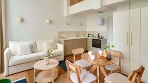 Una sala de estar moderna con sofá, mesa de comedor y sillas. Hay una zona de cocina con armarios y encimera.