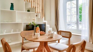 Un comedor con una mesa redonda de madera, cuatro sillas acolchadas y un televisor sobre un estante blanco.