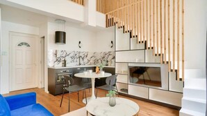 A modern living room with a blue sofa, a marble coffee table, and a kitchen area with a marble backsplash and wooden accents. - Perchoir Parisien - Dupleix avec mezzanine pour 4 (Paris)