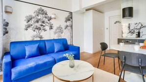 A modern living room with a blue sofa, a round coffee table with a vase, and a wall mural. - Perchoir Parisien - Dupleix avec mezzanine pour 4 (Paris)