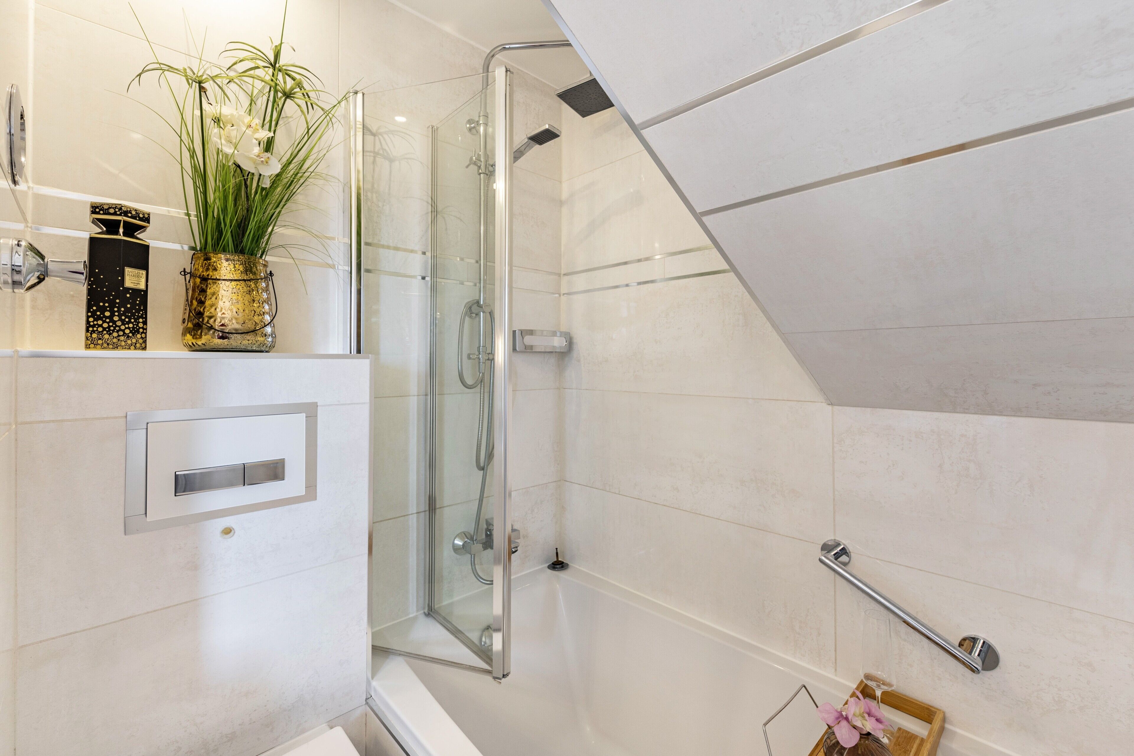 Un baño moderno con cabina de ducha de vidrio, pared con azulejos blancos, estante con adornos y barra de apoyo.