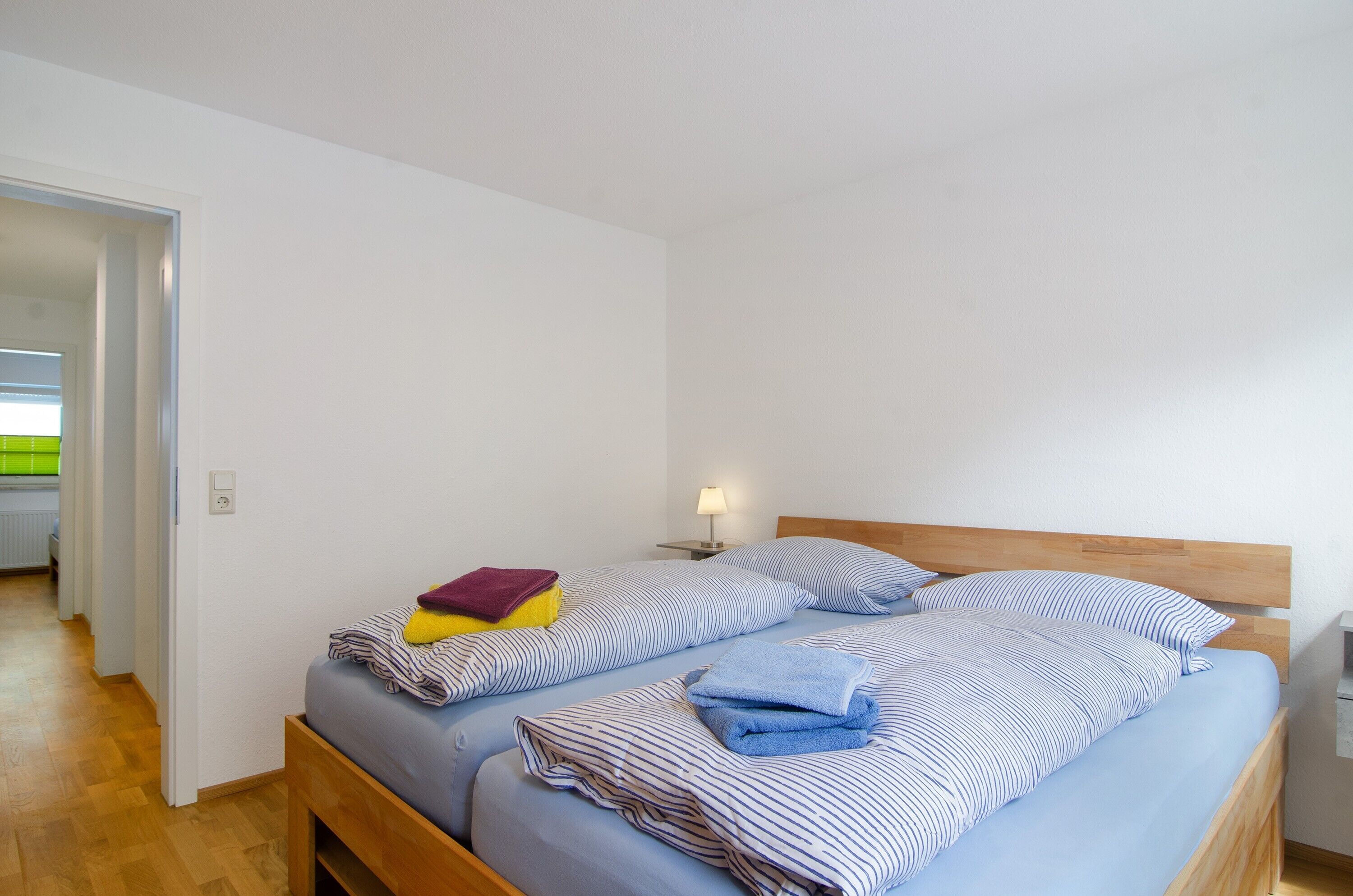 A bedroom with two beds, a nightstand, a lamp, and a wooden floor.