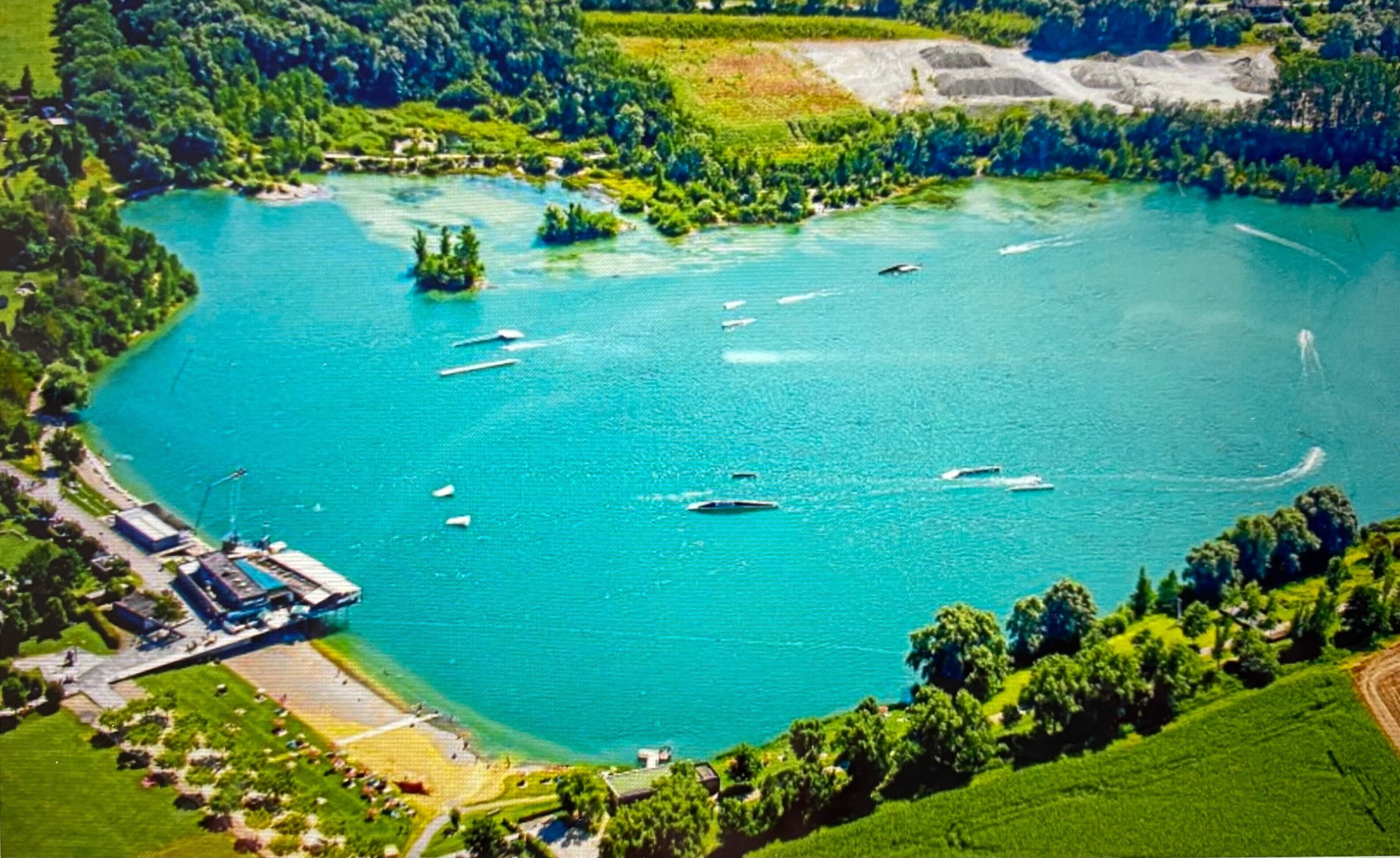 An aerial view of a lake surrounded by greenery, boats, and a dock area.