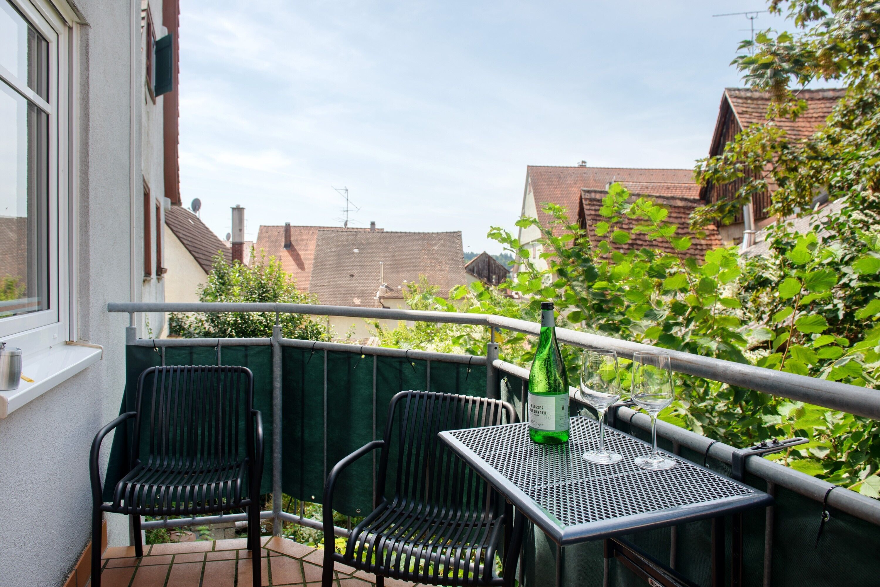 Un balcon avec deux chaises, une table et une bouteille de vin.
