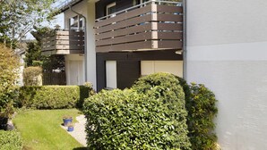 A two-story residential building with a balcony, a well-maintained garden, and a garage.