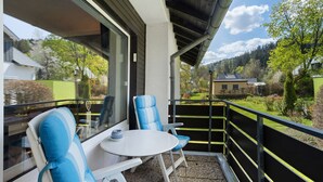 A balcony with two blue-striped chairs and a small table, overlooking a green landscape and houses.