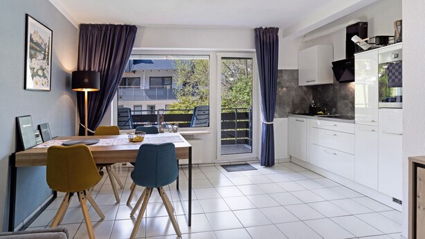 A modern kitchen with white cabinets, a dining table with chairs, a lamp, and a view through a sliding glass door to the outside.