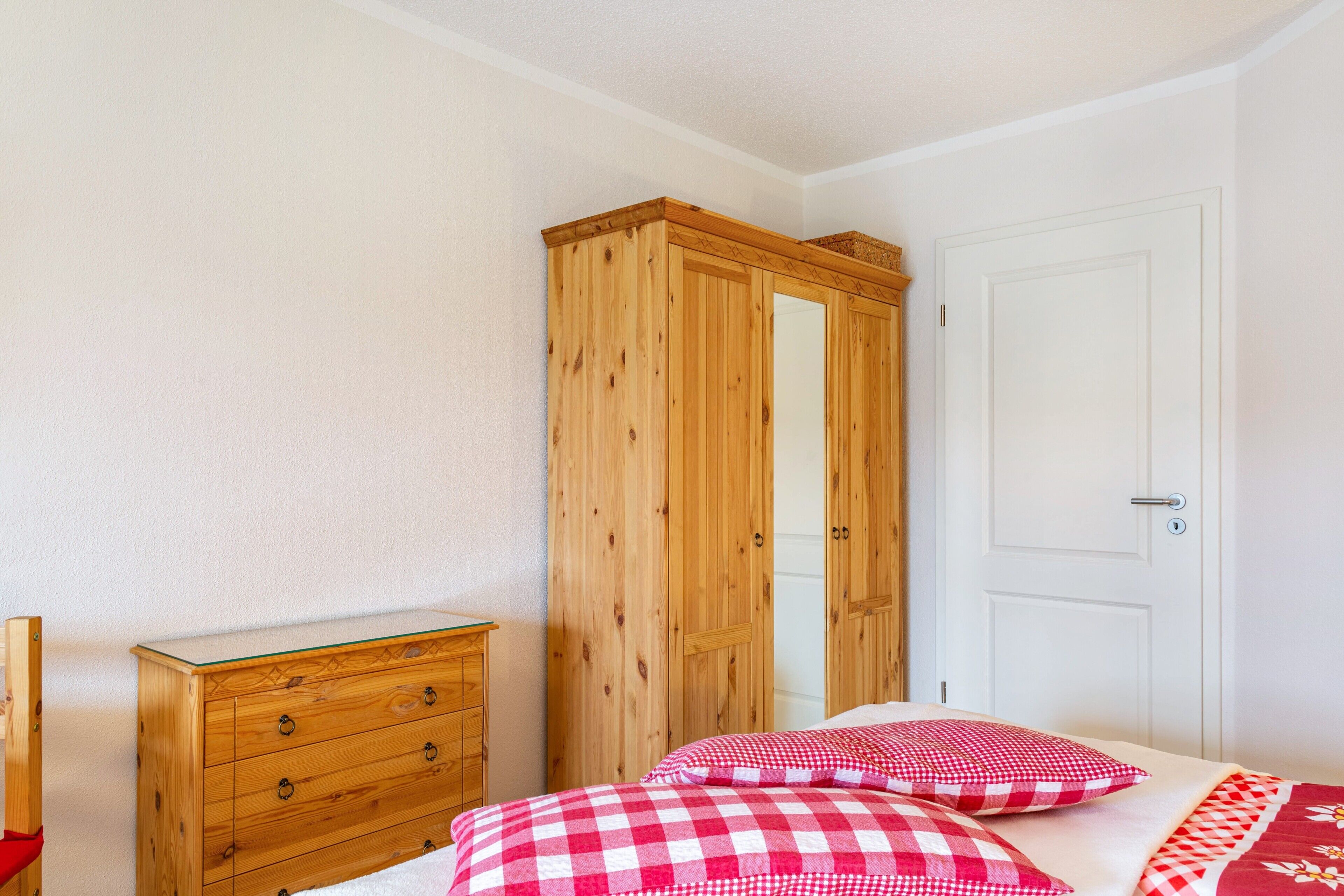 A bedroom with a wooden wardrobe, a dresser, and a bed with checkered bedding.