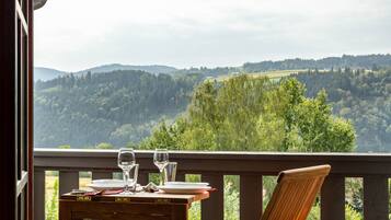 Une table à manger avec des verres et des assiettes, une chaise, et une vue sur une vallée boisée.