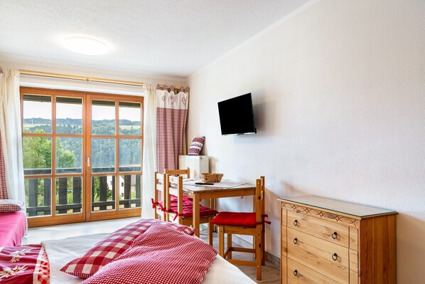 Ein Schlafzimmer mit Bett, Schreibtisch, Stuhl, Fernseher und Blick ins Freie.