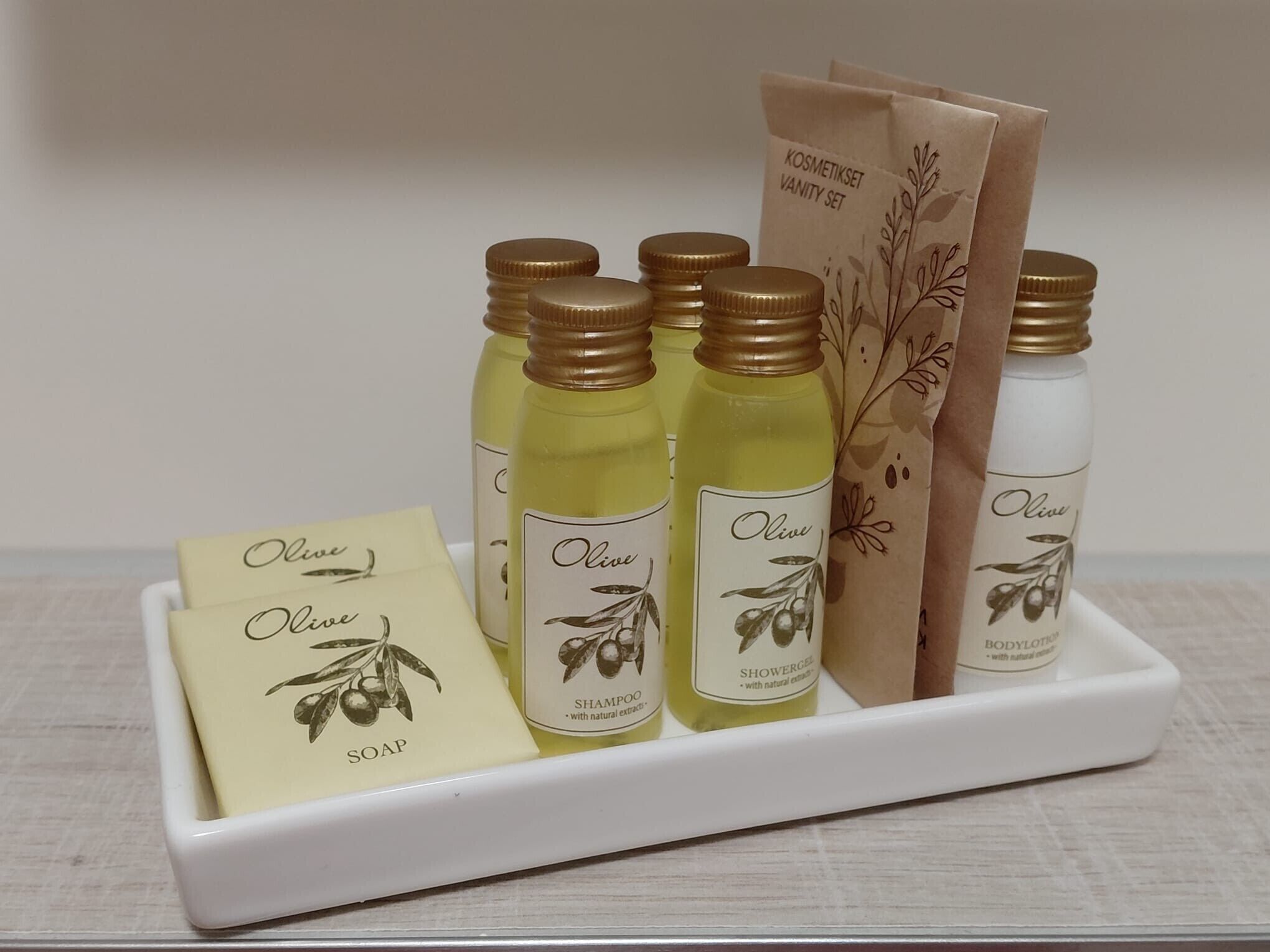 A set of olive-based personal care products including shampoo, shower gel, soap, and lotion, arranged on a white tray.