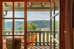 Ein Balkon mit Holzstuhl und Tisch, der Blick auf eine bewaldete Landschaft bietet.